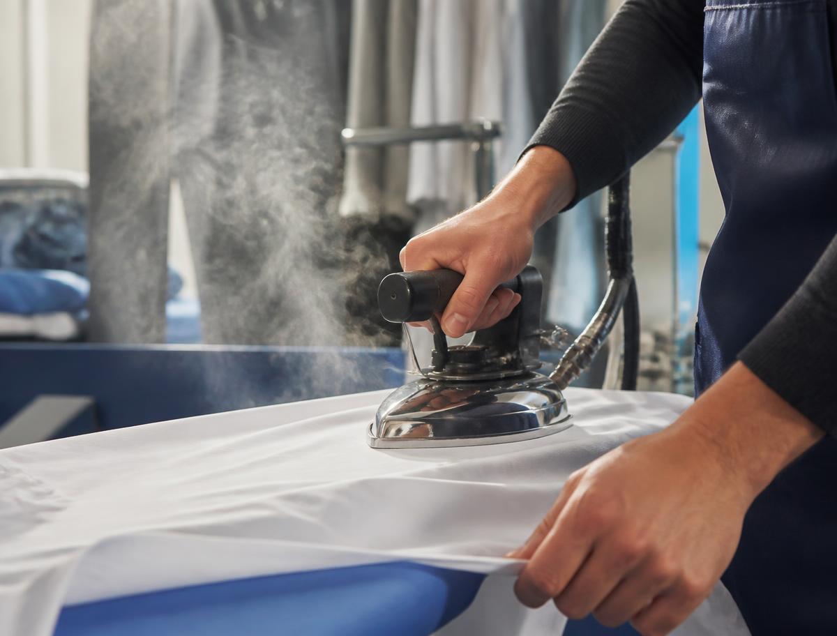 Manos profesionales planchando una camisa blanca